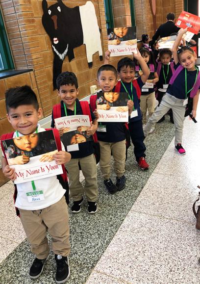 a line of small latino children pose for a picture with their books. they are smiling.