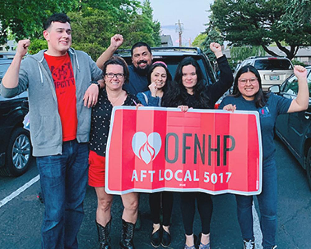people stand with their fist up behind a sign that reads "OFNHP AFT Local 5017"